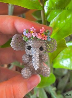 a tiny beaded elephant with flowers on its head is held by someone's hand