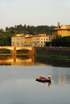 a small boat floating on top of a lake next to a bridge with buildings in the background