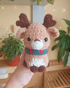 a hand holding a small crocheted stuffed animal in front of a potted plant