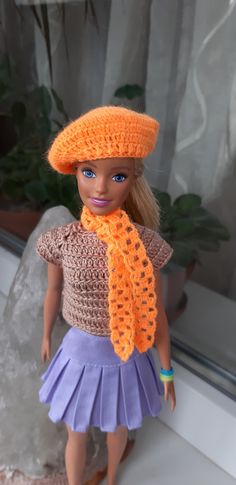 a doll wearing a crocheted hat and purple skirt is standing in front of a window