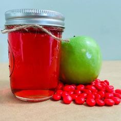 a jar of red liquid next to a green apple and some beans on a table