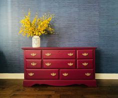 a vase with yellow flowers sitting on top of a red dresser next to a blue wall