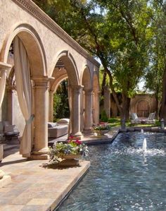 an outdoor swimming pool surrounded by trees and arches with water running through the center area