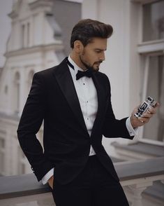 a man in a tuxedo looking at his cell phone while standing on a balcony