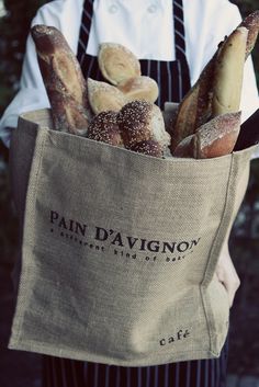 a person wearing an apron holding a bag full of bread and pastries in it