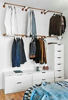 an organized bedroom with clothes hanging on the wall and dressers in front of it