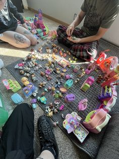 two people sitting on the floor with toys all over their feet and one person standing in front of them