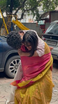 a woman in a yellow and pink sari hugging another woman's head on the street