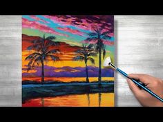 a person is holding a paintbrush in their hand and painting a sunset with palm trees