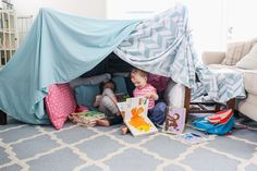 two children are sitting under a tent with books in front of them on the floor