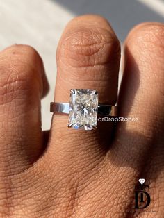 a woman's hand with a diamond ring on top of her finger, showing the center stone