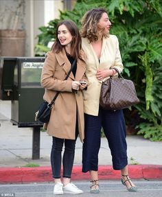 two women standing next to each other in front of a mailbox on the street