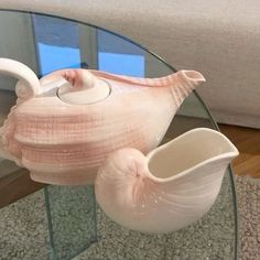 a glass table topped with a vase next to a white swan shaped container on top of a glass table