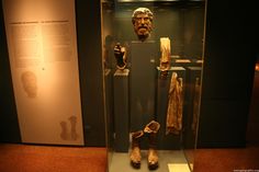 some ancient artifacts are on display in a glass case with other items behind it, including shoes and scarves