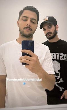 two men standing in front of a mirror taking a selfie with their cell phone