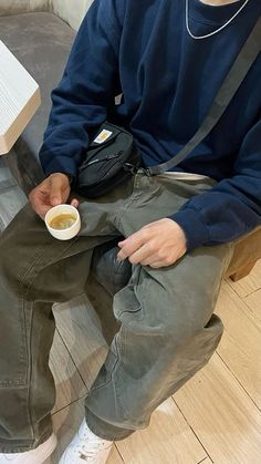 a man sitting on the floor holding a coffee cup in his hand and looking down