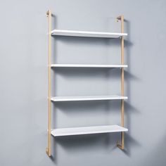 three white shelving shelves against a gray wall with wooden dowks on each shelf