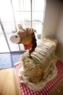 a stuffed horse is sitting on hay bales in front of a window with a red and white checkered tablecloth