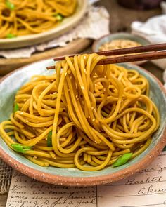 a bowl full of noodles with chopsticks sticking out of the top and another bowl in the background