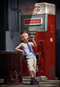 a young boy standing in front of a coca - cola machine talking on his cell phone