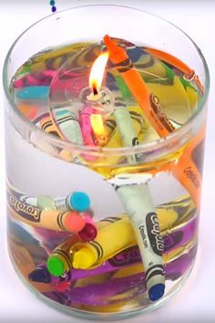 a glass container filled with lots of crayons and a lit candle in it