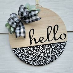 a wooden sign with the word hello painted on it and a black and white bow