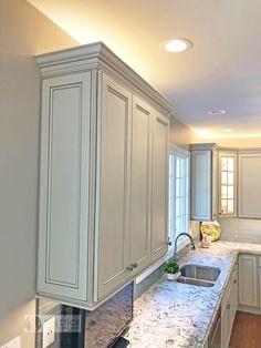 a kitchen with white cabinets and marble counter tops in the middle of it is lit by recessed lights