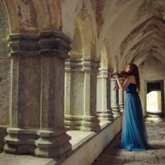 a woman in a blue dress is playing the violin inside an old building with columns and arches