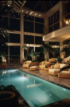 an indoor swimming pool with lounge chairs and plants in the background, at night time