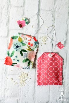 two baby bibs hanging on a white brick wall with flowers and leaves around them