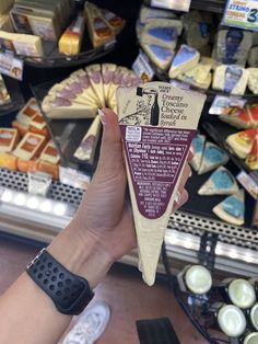 a person holding up a piece of cheese in front of some other food items at a store