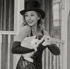 a woman in a hat and dress holding a cat