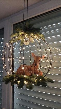 a deer is sitting in the center of a christmas decoration hanging from a window sill