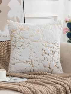 a white and gold pillow sitting on top of a couch next to a vase with flowers