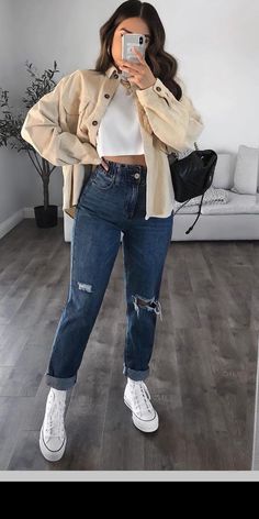 a woman taking a selfie while wearing ripped jeans and a white cropped top