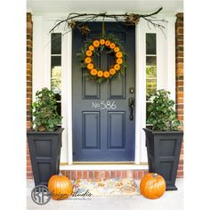 two pumpkins sitting in front of a blue door with a wreath on the side