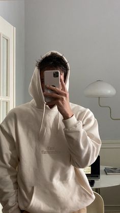 a man in a white hoodie taking a selfie with his cell phone while wearing khaki pants