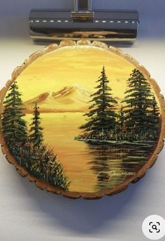 there is a painting on the back of a wooden plaque that has trees and mountains painted on it