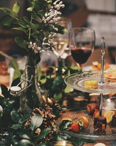 an assortment of food and drinks on a table with greenery, wine glasses and flowers