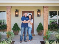 a man and woman standing in front of a house with their arms around each other