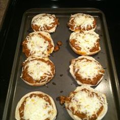 six mini pizzas sitting on top of a baking pan covered in cheese and sauce