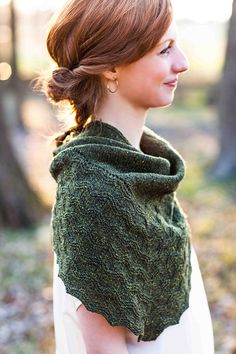 a woman standing in the woods wearing a green shawl and white dress with her hair pulled back