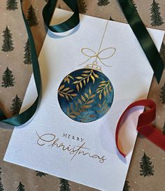 a christmas ornament hanging from a ribbon on top of a card with the words merry christmas