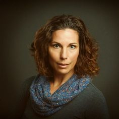 a woman with curly hair wearing a blue scarf and posing for a photo in front of a dark background