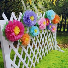 colorful paper flowers are hanging on a white fence