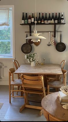 a kitchen table and chairs in front of a window with wine bottles hanging on the wall