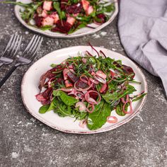 two plates filled with salad on top of a table next to utensils and silverware