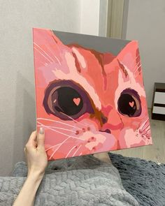 a person holding up a painting with a cat's face painted on the canvas