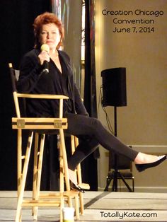 a woman sitting in a chair with her legs crossed while talking into a microphone on stage