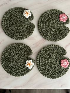 four crocheted coasters with flowers on them sitting on a marble counter top